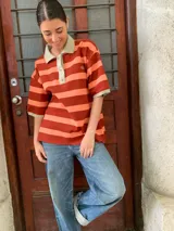 Remerón de algodón a rayas horizontales color naranja y salmón, con cuello tipo polo y mangas cortas.