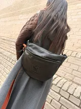 Riñonera de tamaño XL en color marrón chocolate, con diseño exterior trenzado y un parche frontal con monograma grabado. Cuenta con cierre diagonal y correa regulable.