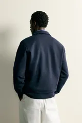 Sudadera polo de corte regular, confeccionada en tejido técnico interlock de algodón con elasticidad. Presenta cuello solapa, cierre frontal de cremallera y manga larga con puños acabados en rib.