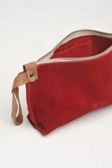 Sobre de mano rojo de gamuza con cierre de cremallera y correa de cuero marrón.