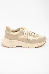 Zapatilla urbana de diseño chunky, confeccionada en una combinación de cuero liso y gamuza en tonos beige y arena. Presenta cordones al tono, suela de plataforma con relieve y detalle de marca grabado en el talón.