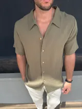Camisa de manga corta en tejido de muselina color verde militar, con cuello solapa y cierre frontal de botones.