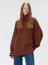 Pullover de punto color rojo, con cuello tortuga, corte holgado y mangas largas con puños acanalados en contraste con rayas blancas. Presenta un logo bordado en el pecho.