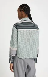 Camisa de algodón con estampado de rayas diagonales en tonos verdes y beige, corte recto y amplio. Presenta cuello clásico estructurado, mangas largas con puños anchos y cierre frontal de botones. Incluye una corbata a juego con rayas verticales en contraste.
