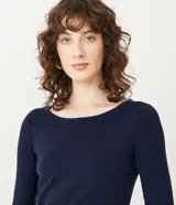 Suéter de punto color rosado, con cuello barco, mangas largas y puños con botones decorativos. El dobladillo también es acanalado.