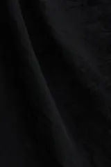 Vestido corto negro con tiras halter finas, escote con volado amplio y bajo asimétrico con volado y cordón colgante.