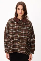 Chaqueta de corte holgado con estampado de cuadros en tonos marrones, blancos y negros. Presenta cuello de pana en color marrón oscuro, cierre frontal con botones metálicos y bolsillos laterales amplios.