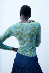 Jersey de punto Zara con cuello redondo y manga larga, con estampado floral a contraste en tonos verdes y morados sobre base celeste.
