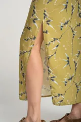 Falda midi color verde oliva con estampado de ramas en negro y blanco. Tiene corte evasé, cintura alta con cordón ajustable y abertura lateral.