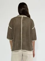 Chaqueta de punto calado en color negro con detalles de bordes en color crudo. Presenta cuello camisero, cierre frontal con botones, mangas cortas y un bolsillo frontal tipo parche.
