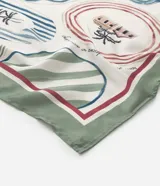 Pañuelo de satén con estampado tropical que incluye palmeras, casas, olas y otros íconos que recuerdan a las brasilidades. Presenta un borde verde y detalles en rojo, azul y rosa.