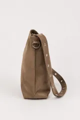 Bolso tipo shopper de gamuza marrón, con asa de hombro ajustable decorada con ojales metálicos plateados y hebilla lateral.