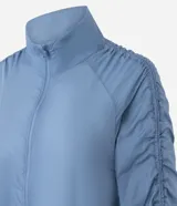 Campera deportiva tipo parka de microfibra en color azul, con cuello alto, cierre frontal por cremallera y mangas largas con puños elásticos. Presenta un diseño con fruncido lateral ajustable y corte amplio.