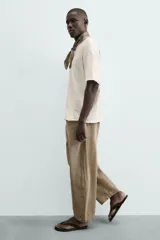 Jeans de hombre, tiro medio, color marrón claro o caqui, con corte relaxed fit y perneras anchas. Presenta cinco bolsillos y costuras laterales giradas hacia el frente.