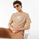 Remera color beige con estampado blanco en el frente que incluye un diseño gráfico de sol, olas y palmeras, y el texto 'Chill Zone Ahead'.