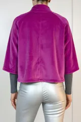 Chaqueta de terciopelo color fucsia, de corte recto y diseño corto. Presenta cuello alto, cierre frontal con botones y bolsillos laterales ocultos.