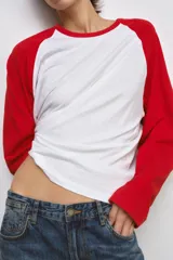 Camiseta de manga larga con diseño ranglan, cuerpo en color blanco y mangas en color rojo. Presenta cuello redondo y bajo recto.