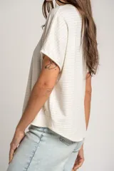 Remera oversize color crudo con sutiles rayas horizontales plateadas, mangas cortas caídas y cuello redondo.