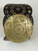 Cinto faja de cuero sintético negro con hebilla metálica dorada con diseño circular calado.