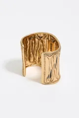 Pulsera brazalete rígido de metal dorado con diseño de líneas verticales en relieve y detalles de esmalte negro.