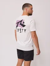 Remera blanca de algodón con estampado gráfico en la espalda. El diseño presenta el logo de Rusty en negro sobre un fondo rectangular lila, con tipografía angular.