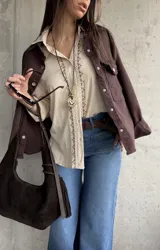 Camisa beige de tejido liviano y calce relajado, con manga larga y detalle de puntilla y bordado en contraste que recorre el frente.