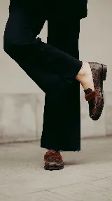 Mocasín de cuero con textura gastada, color marrón, con detalle de pelo en la parte superior y suela plana.