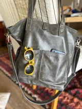 Cartera tipo tote bag color gris grafito, con doble asa de mano y correa bandolera extraíble y ajustable. Incluye dos bolsillos externos grandes.
