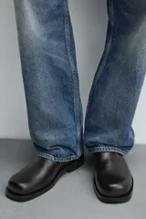 Bota de piel negra con diseño minimalista, cierre de cremallera lateral, horma cuadrada y suela a tono con ligero tacón.