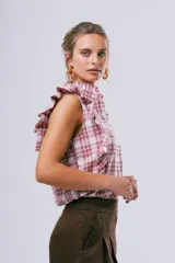 Blusa sin mangas color blanco con cuello alto con volados y detalles de volados en los hombros. Cuenta con cierre frontal de botones.