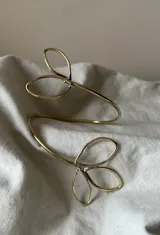 Brazalete abierto de bronce dorado con diseño de hojas estilizadas en los extremos.