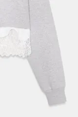 Sudadera crop de cuello redondo y manga larga con puños elásticos. Presenta un diseño de doble capa con un top interior satinado y un bajo decorado con encaje a tono.