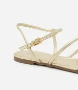 Sandalia plana dorada con tiras finas y cierre con hebilla en el tobillo.