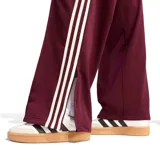 Pantalon deportivo Adidas modelo Firebird, color bordó, con diseño de pierna recta, cintura elástica, bolsillos laterales con cierre y las icónicas tres tiras blancas en los laterales.