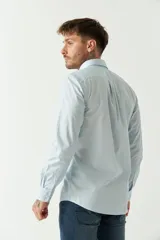 Camisa celeste de manga larga con logo bordado y bolsillo en el pecho.