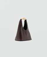 Bolso de mano tipo hobo, confeccionado en poliuretano color marrón oscuro con acabado liso. Presenta un diseño minimalista con una estructura rígida y un asa superior metálica en tono dorado.