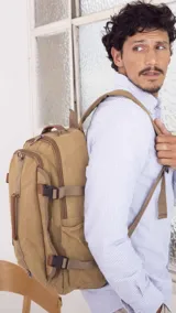 Mochila de tela canvas color beige con detalles en símil cuero marrón. Tiene presillas y broches plásticos para ajustar, bolsillo frontal con cierre, repartición interna para laptop, bolsillos laterales, correas cortas para usar como bolso de mano y correas regulables para la espalda.