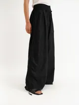 Pantalón negro de lino con cintura elástica fruncida y pernera ancha, con detalles de cordones ajustables a los lados.