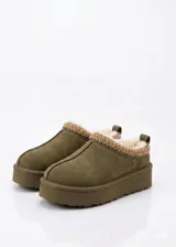 Zueco de gamuza color verde oliva con interior forrado en piel sintética. Presenta una suela de plataforma y un detalle de bordado geométrico en el borde superior.