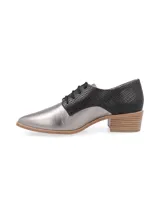 Zapato acordonado de estilo oxford con diseño bicolor. Presenta una puntera y lateral en cuero metalizado plateado, mientras que la parte trasera y el área de los cordones están confeccionados en cuero con textura de reptil en color negro. Incluye un taco bajo de madera y suela a tono.