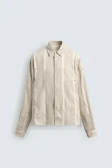 Camisa de corte relajado confeccionada en una mezcla de algodón y lino con textura semitransparente. Presenta un diseño de rayas verticales, cuello solapa, manga larga con puños abotonados y cierre frontal con botones.