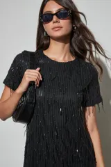 Vestido corto negro con lentejuelas y flecos colgantes, de manga corta y cuello redondo.
