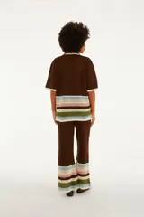 Pantalón de punto color marrón, de corte recto y tiro medio, con cintura elástica. Presenta diseño calado y franjas horizontales de colores en la parte inferior de las piernas.