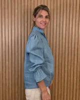 Blusa rosada de algodón con delicados bordados florales blancos, escote en V con cuello elevado y volados, y mangas largas con puños acampanados.