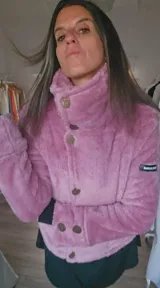 Campera corta de piel sintética en color rosa, con cuello alto envolvente y cierre frontal mediante botones dispuestos en diagonal. Presenta un diseño de textura suave y voluminosa con un parche decorativo en la manga.