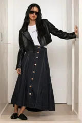 Maxi falda de jean en color azul oscuro, con cierre frontal de botones metálicos y costuras pespunteadas visibles. Tiene diseño evasé que aporta movimiento y caída fluida.