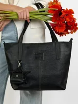 Cartera tote de cuero genuino color negro, con costuras visibles a contratono, asas dobles para hombro, parche frontal con logo grabado y charms colgantes en forma de estrella y mini monedero.