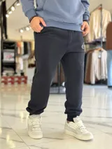 Pantalón jogger negro de corte oversize con felpa, bolsillos laterales y puños elásticos en los tobillos. Presenta un pequeño logo estampado en color blanco en la pierna izquierda.