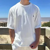 Remera de tejido de punto con textura acanalada horizontal, color blanco, de corte oversize y manga corta. Presenta un pequeño logo bordado en el pecho.