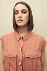 Chaleco color salmón con cuello camisero, sin mangas, cierre frontal con botones a tono y bolsillos de parche en el pecho. Incluye cinturón de la misma tela para ajustar a la cintura.